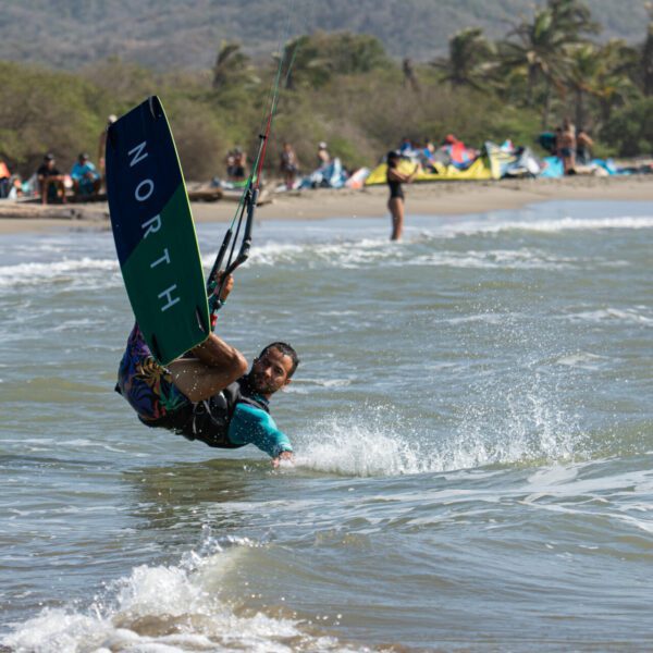 Kite Explorer Colombia - Kite Surf - Colombie - figure de kitesurf, le pratiquant de kite a sa planche en l'air et la tête en bas, il touche l'eau avec son bras, la plage est visible au loin