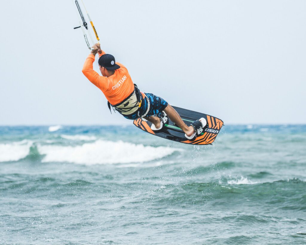 kitesurfer en plein saut en kite, en pleine journée, il est de dos et porte un lyvra orange