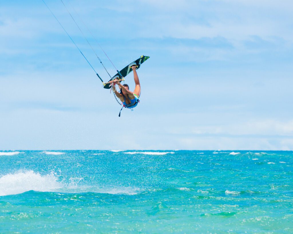 jeune femme en train de faire du kite surf et d'effectuer un saut , au dessus d'une mer bleue turquoise